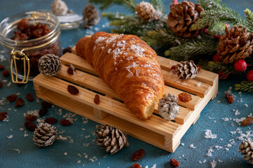 Croissant close-up on a wooden board with spruce branch and cones