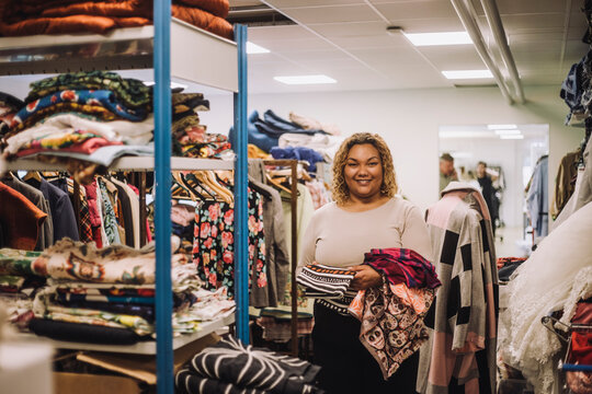 Portrait of smiling female fashion designer holding fabrics while standing at workshop