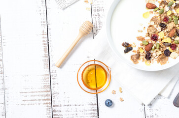 Healthy breakfast: Yogurt with homemade whole grain muesli or granola in a white bowl with honey and coffee on the white table.