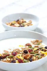 Healthy breakfast: Yogurt with homemade whole grain muesli or granola in a white bowl with honey and coffee on the white table.