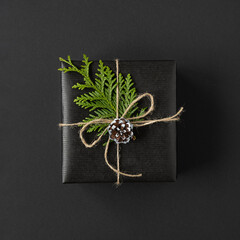 Black gift box tied with rope, cone and green sprig of thuja on dark background. Top view.