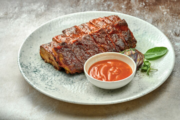 Baked barbecue ribs with mango sauce in a white plate on a textured background. Close-up, selective focus