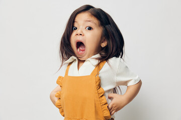 a cute little girl of preschool age is standing in an orange dress on a white background with her...