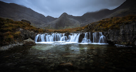 A very dark and moody Fairy pools, Isle of Skye.  Waterfalls in front of towering mountains