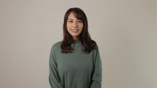 Beautiful asian woman smiles. White wall.