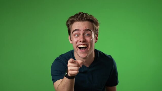 Slow motion portrait of hipster man 20s laughing pointing finger at camera isolated on green screen chroma key background studio portrait