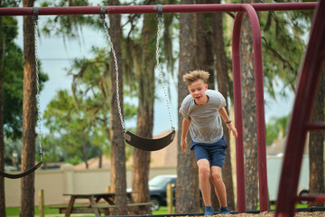 Young handsome smiling teenage boy jumping out of the swings on summer vacations sunny day. Danger of accident concept