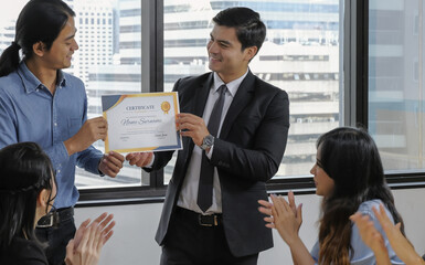 Young caucasian manager in suit giving mock up certificate to asian staff with happy smiling face while others applauding for congratulation in office meeting room. Selective focus. - obrazy, fototapety, plakaty
