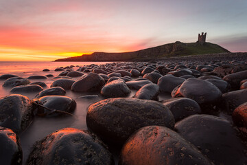 Dunstanburgh Castle, North West England during a fiery sunrise.  Northumberland Heritage and history. 