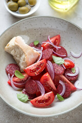 Close-up of salad with red tomatoes, fried chorizo and red onion served in a beige plate, vertical shot, selective focus