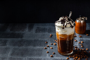 Cold coffee drink frappe (frappuccino), with whipped cream and chocolate syrup, with straws, coffee beans on a dark gray stone table, copy space  - obrazy, fototapety, plakaty