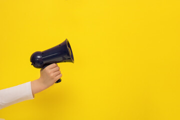 children's hand holding a megaphone on a yellow background with copy space