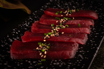 Sashimi tuna, delicious Japanese food with black background and decorated with leaves and soy sauce, for oriental and Asian food restaurant.