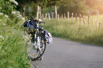 Bicycle with electric motor stands on a road leading through green nature. The bicycle has several...