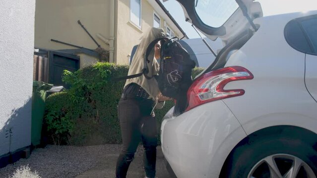 Woman loading backpack and helmet into cat trunk in font of house