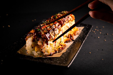 Japanese sushi food volcano roll with black background for oriental and Asian food restaurant with zenithal light. The customer eats with chopsticks. © Alberto Cotilla