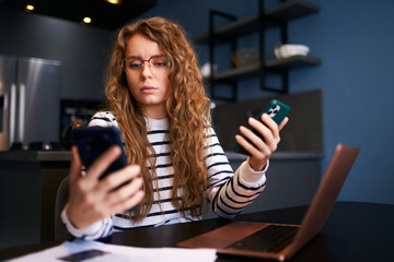 Curly blonde woman in glasses working from home with multiple electronic internet devices....