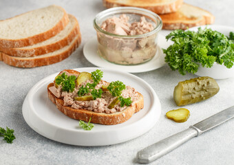 Cod liver in a jar and sandwich with liver, pickled cucumber and parsley on a white plate on a gray concrete background. Breakfast, brunch. Natural source of omega 3 and vitamin D. Selective focus