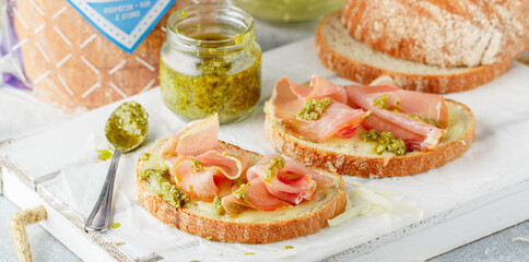 Whole grain bread bruschetta with mozzarella cheese, ham and green pesto sauce made of parmesan cheese, fresh basil, garlic and olive oil. Breakfast, brunch. Selective focus, banner