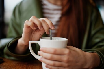 Woman in cafe stirring sugar in white coffee mug, autumn vibe and warmth