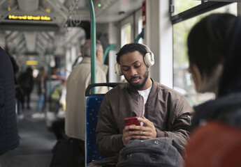 young man in the tram uses a smartphone - obrazy, fototapety, plakaty