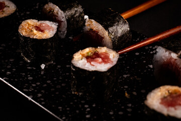 Tuna maki, Japanese sushi, delicious Japanese food with black background and decorated with chopsticks and a bowl of soy sauce, for oriental and Asian food restaurant.