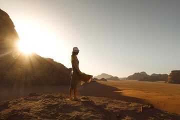 Young woman stand enjoying peaceful moment of beautiful colorful sunrise in desert breeze with sunflare over cliff horizon.Vintage mood, concepts of travel, freedom, happiness, joy