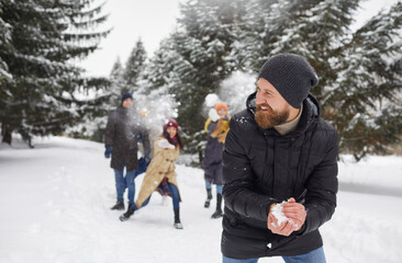Overjoyed diverse young people play snowballs enjoy active winter weekend in forest. Smiling friends laugh relax on frosty snowy vacation or holiday outdoors in park. Friendship and fun.