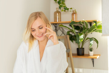 a young blonde girl in the bathroom in a white robe talking on the phone, a relaxed portrait of a girl in a homely atmosphere talking on a smartphone