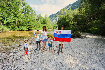 Mother with kids hold slovenian flags in rocky shore of a calm river in Triglav National Park,...