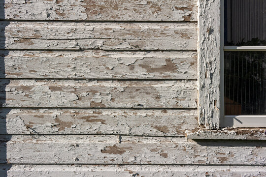 Close Up Texture Background Of An Old Deteriorating 19th Century Barn Wall With Peeling White Painted Wood Siding And Partial View Of A Window