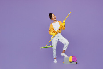 Fototapeta na wymiar Full body side view happy young housekeeper woman wear yellow shirt tidy up hold mop bucket with water wash floor look aside isolated on plain pastel light purple background studio. Housework concept.