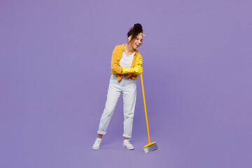 Full body smiling fun young housekeeper woman wear yellow shirt tidy up hold use broom sweeping...