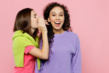 Young two friends fun women 20s wears green purple shirts together whispering gossip and tells secret behind her hand sharing news isolated on pastel plain light pink color background studio portrait