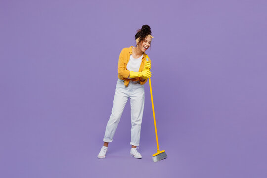 Full Body Smiling Fun Young Housekeeper Woman Wear Yellow Shirt Tidy Up Hold Use Broom Sweeping Brush Look Camera Clean House Isolated On Plain Pastel Light Purple Background Studio Housework Concept