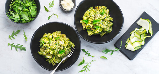 Green vegetarian fusilli pasta with zucchini pesto and herbs on a white marble background in a...