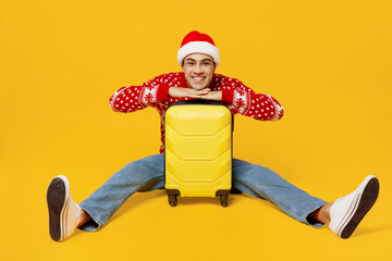 Full body merry traveler man in xmas sweater Santa hat hold suitcase bag isolated on plain yellow background Tourist travel abroad in free spare time rest Air flight trip Happy New Year 2023 concept