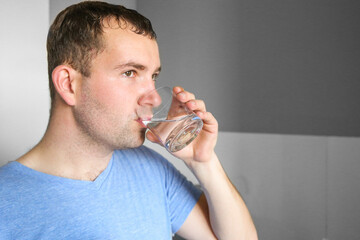 A man drinks water in the kitchen. Glass of water in the morning. Drink water after your workout