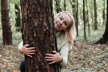 A nature lover hugs a tree trunk in the forest. Green natural background. The concept of people who love nature and protect it from deforestation, pollution or climate change