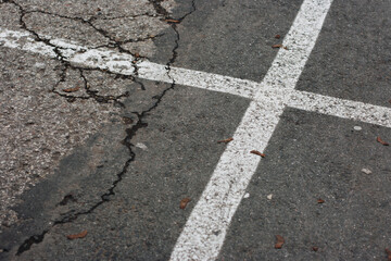 White lines on the cracked asphalt in the parking lot forming a cross. © Emils