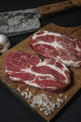 A slice of raw fresh meat on a wooden board on a black background.