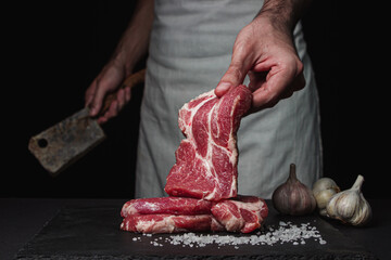 The hand of the cook holds a slice of raw fresh meat on a black background.