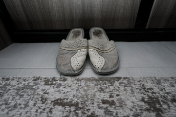 Pair of old grey worn slippers standing on floor of home antechamber near threshold