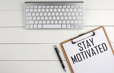 Home office workspace with keyboard, clipboard and pen with text STAY MOTIVATED on white wooden background , business concept