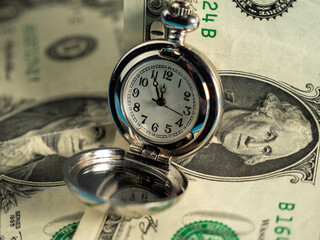 Old pocket watches lie on dollar bills.