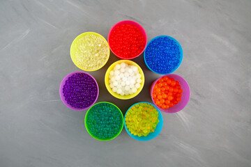 Orbeez toy. Multicolored Hydrogel balls or Water beads in plastic cups on grey background, top...