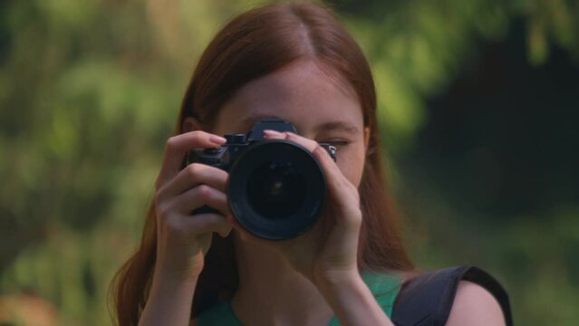 Redhead young girl photographer nature lover using modern camera photographing outdoor. Closeup portrait. Handheld video