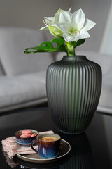 Cup of coffee, sweets,  flowers  on round coffee table. Fashionable interior as background.