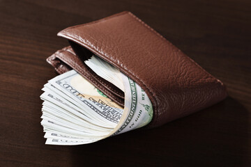 Close-up of a brown leather wallet filled with many hundred dollar bills. Indoors from a high angle view.