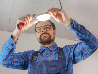 Electrician at work. Service for repair of electrical wiring and replacement of ceiling lamps. builder is installing small lamp on ceiling. Rent-a-gent helps with housework